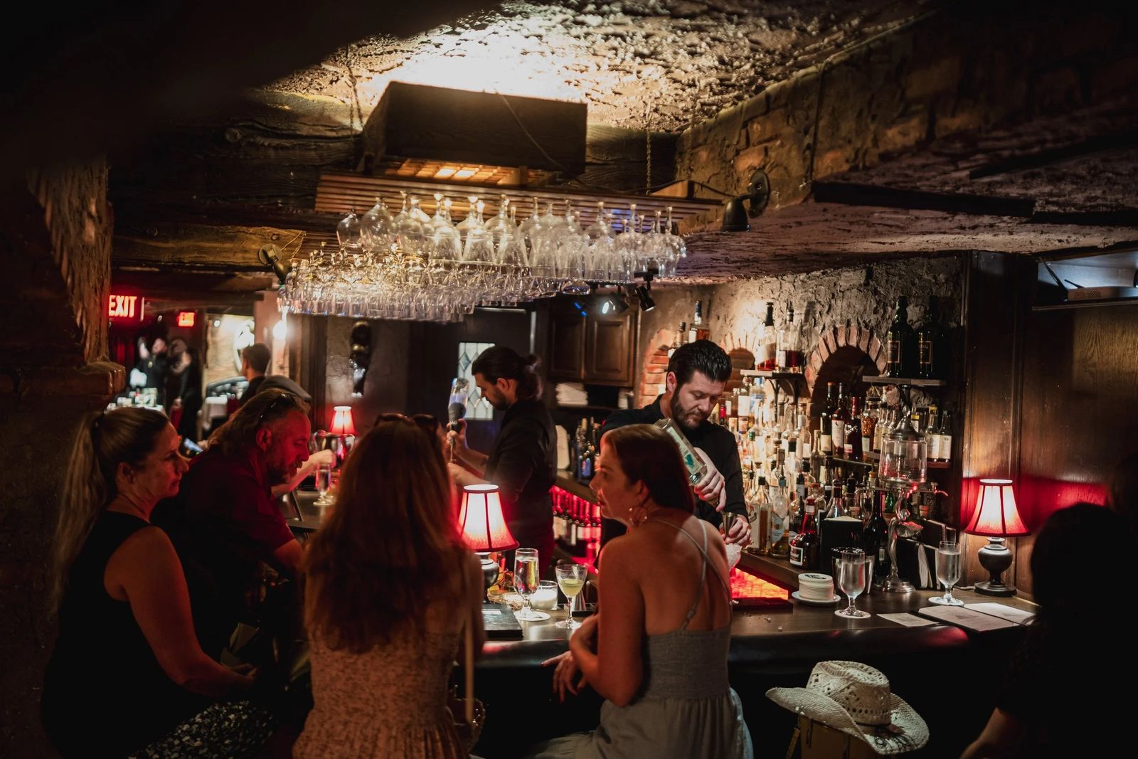 A dim stone-walled bar room with a lit back bar and guests seated along the counter.