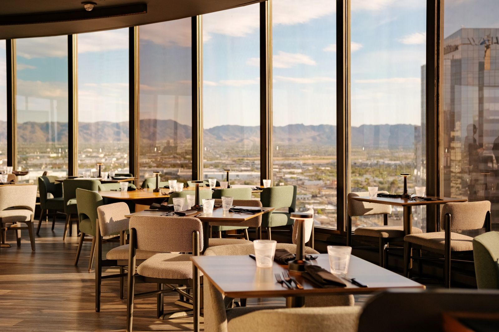 A restaurant dining room with tables and chairs by floor-to-ceiling windows overlooking the city and mountains