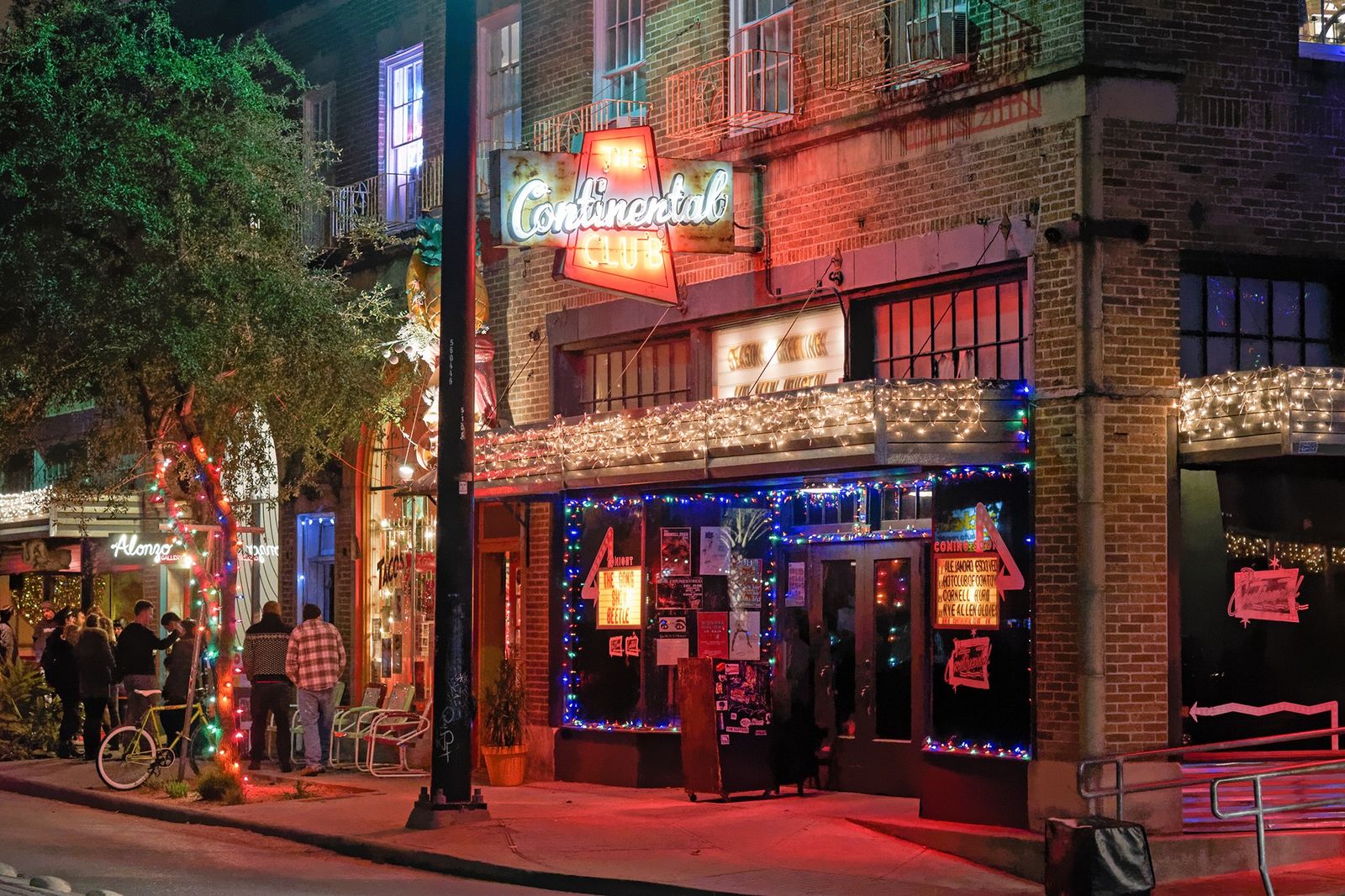 A lit street corner at night with a neon Continental Club sign over a brick storefront and string lights.