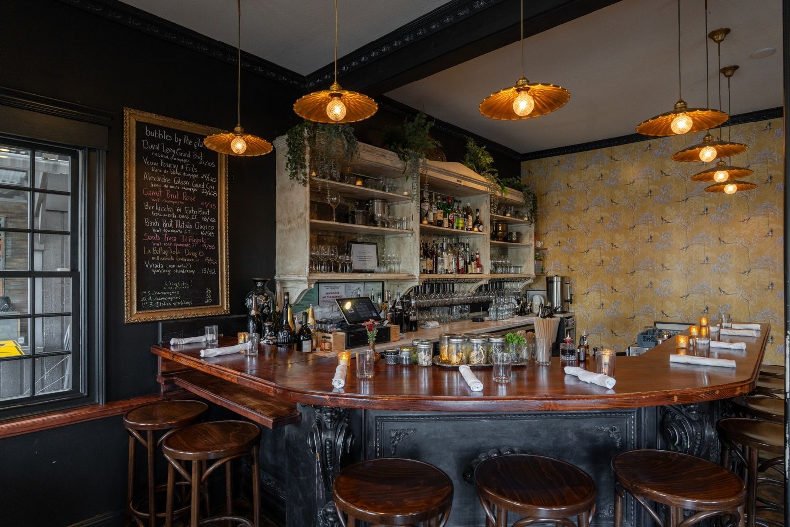A curved wooden bar with stools, pendant lights and shelves of bottles behind it.