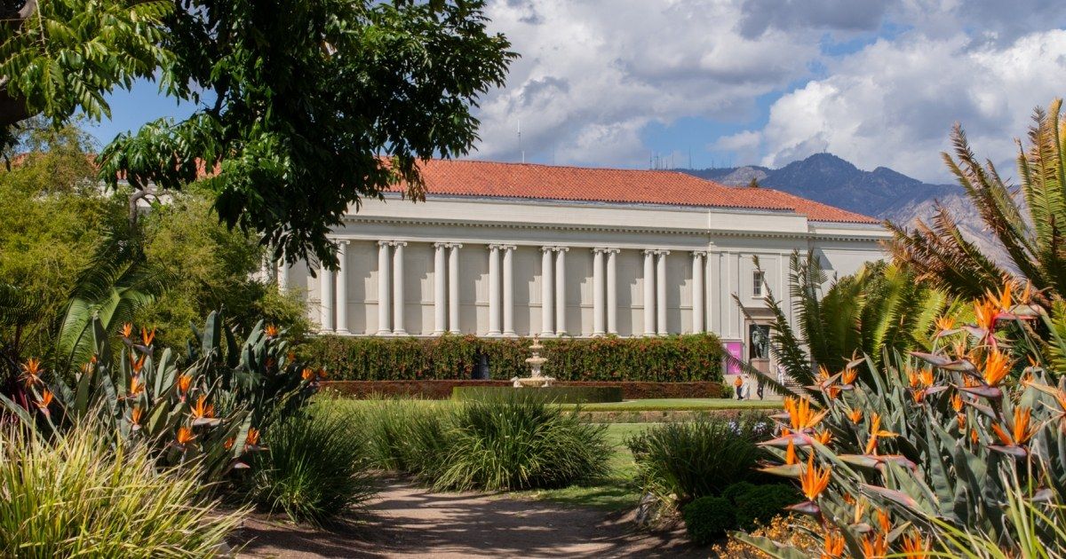 The domed white library building behind gardens of flowers and palms, with mountains in the distance.