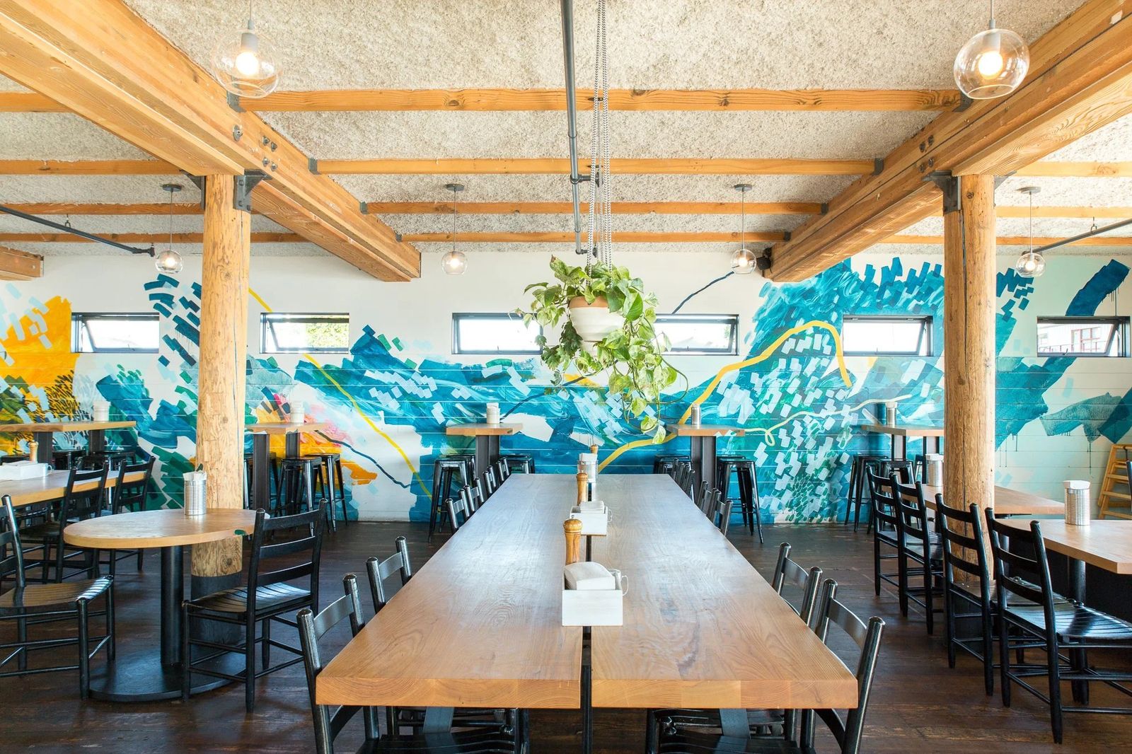 Dining room with long wooden tables, exposed beams and a blue wave mural