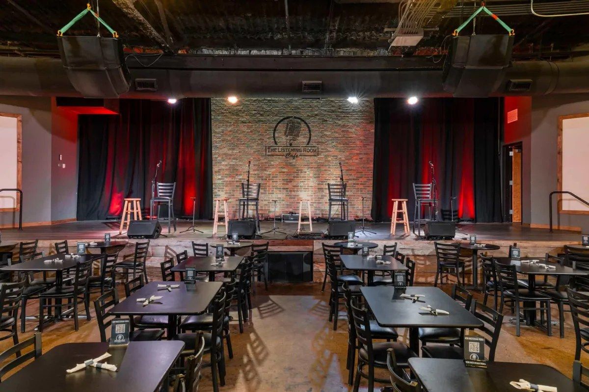Empty music venue with tables and chairs facing a stage with red curtains