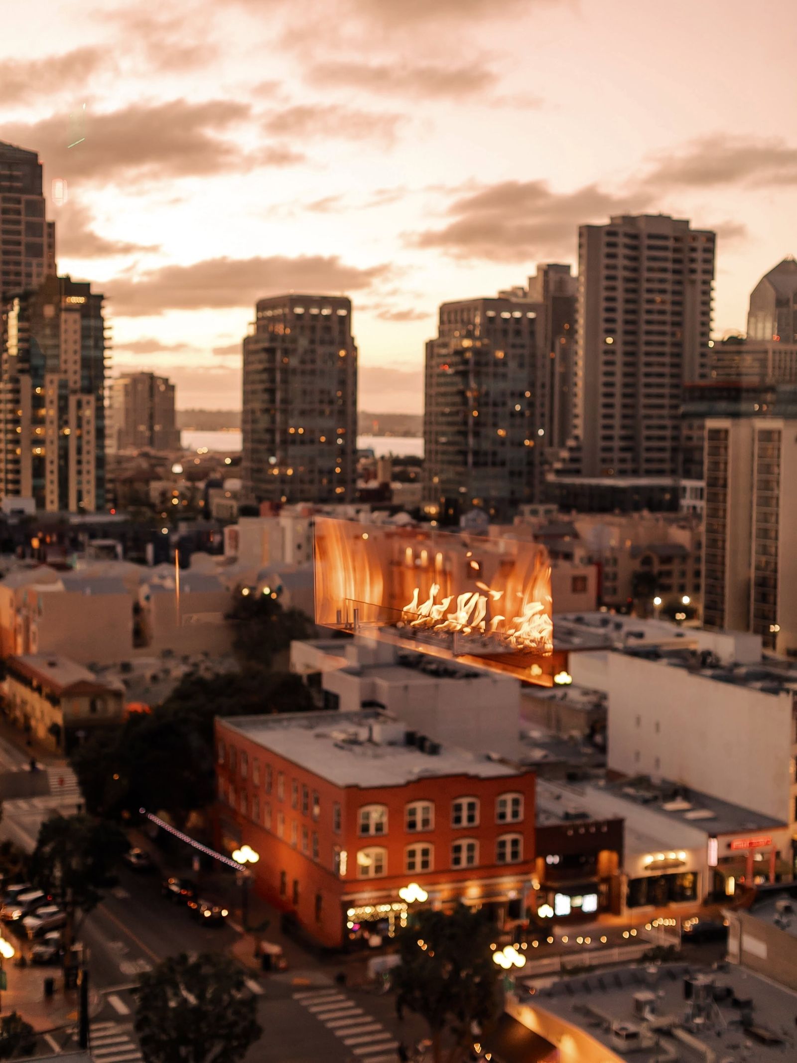A sunset over a city skyline seen from a rooftop, with buildings below in warm light.