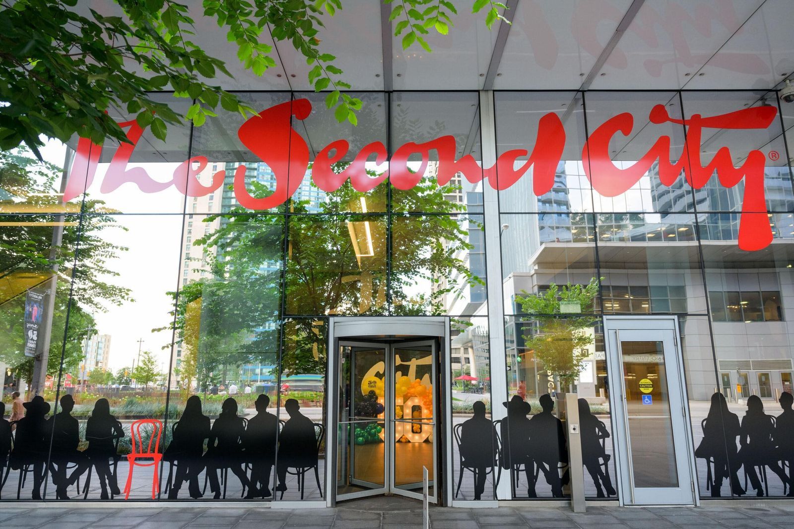 The glass-fronted building with a red Second City sign on its facade, a revolving door and a crowd on the sidewalk below.