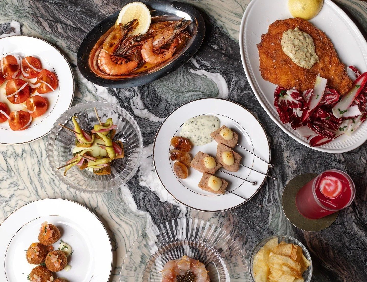 Overhead view of plates of small dishes and a red cocktail on a marble table