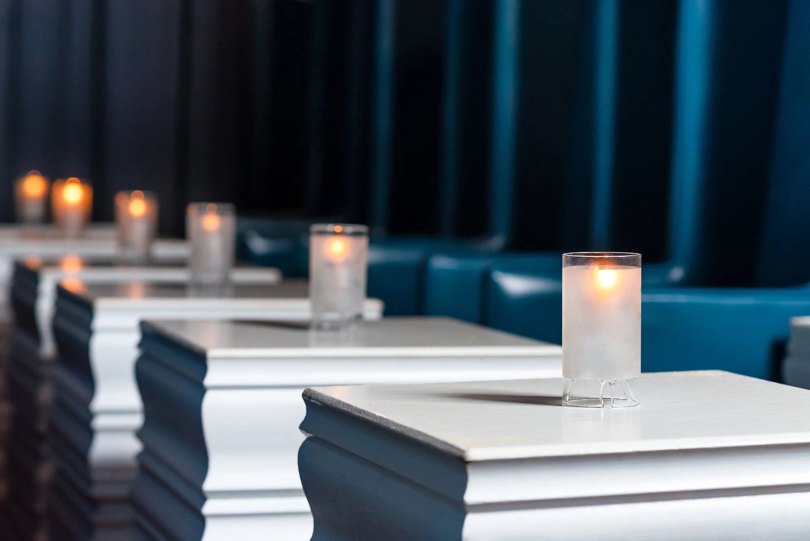 Rows of candlelit white tables beside a deep blue booth in a dim bar.