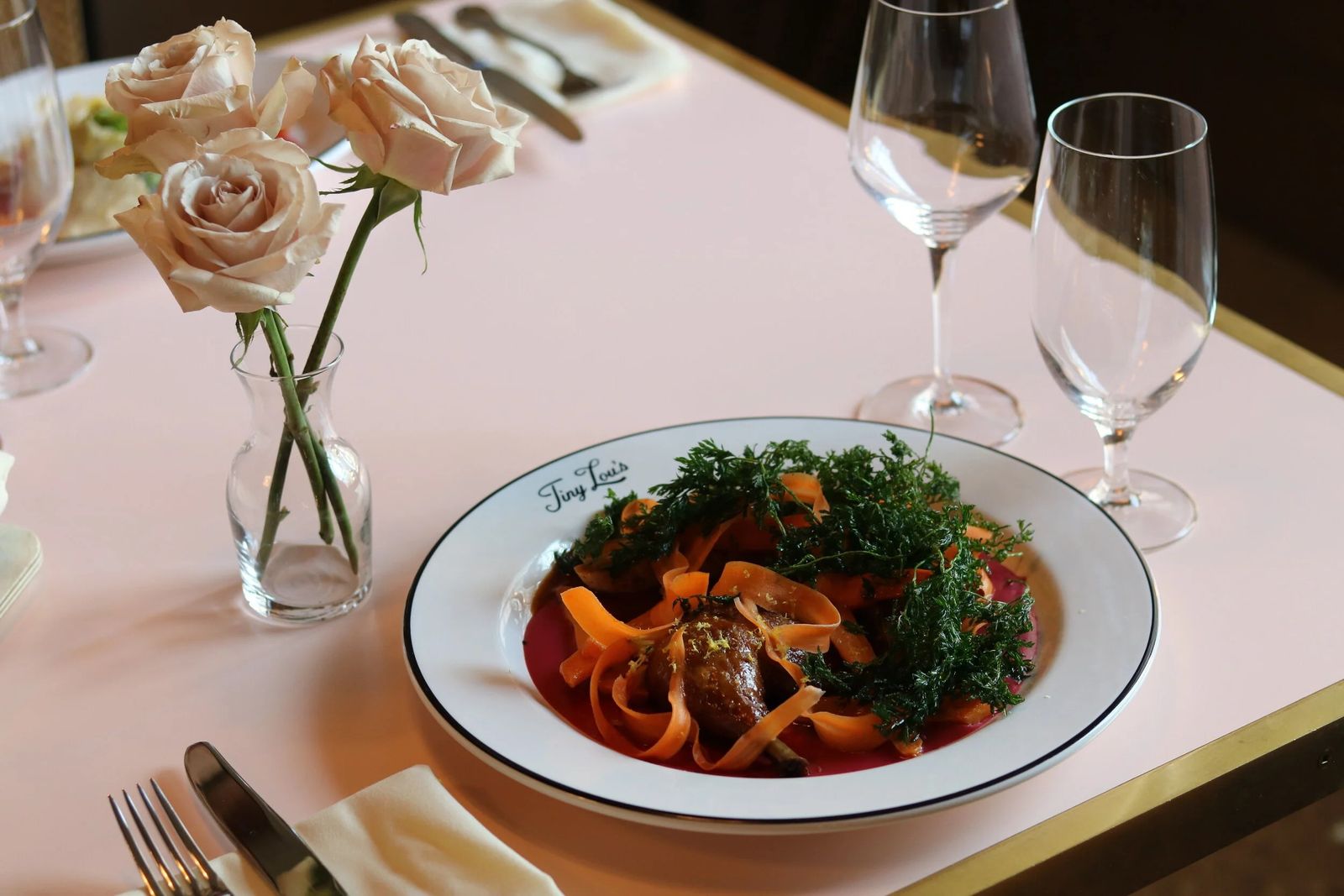 Bowl of pasta on a pink table with roses and wine glasses