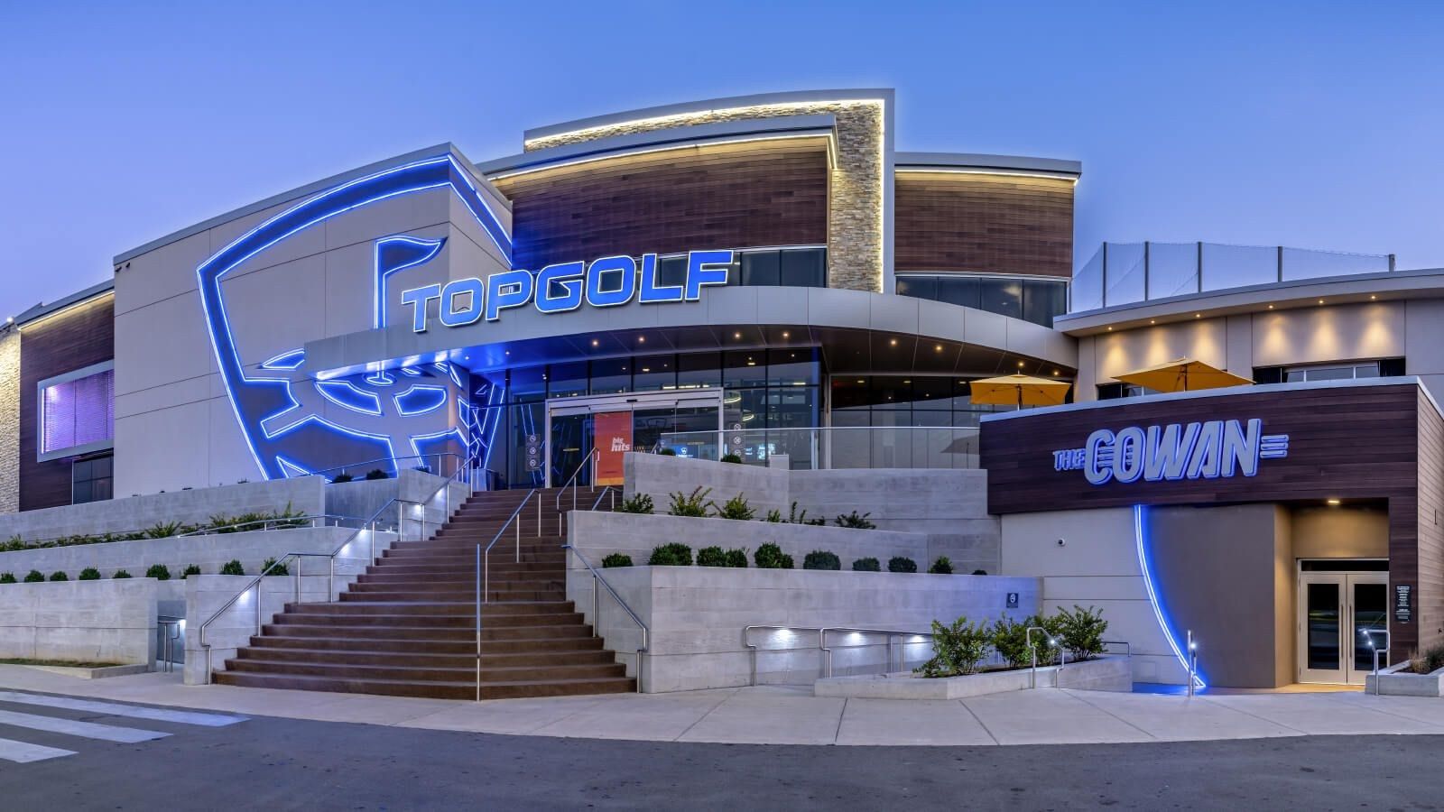 Topgolf venue exterior with staircase and illuminated blue signage at dusk