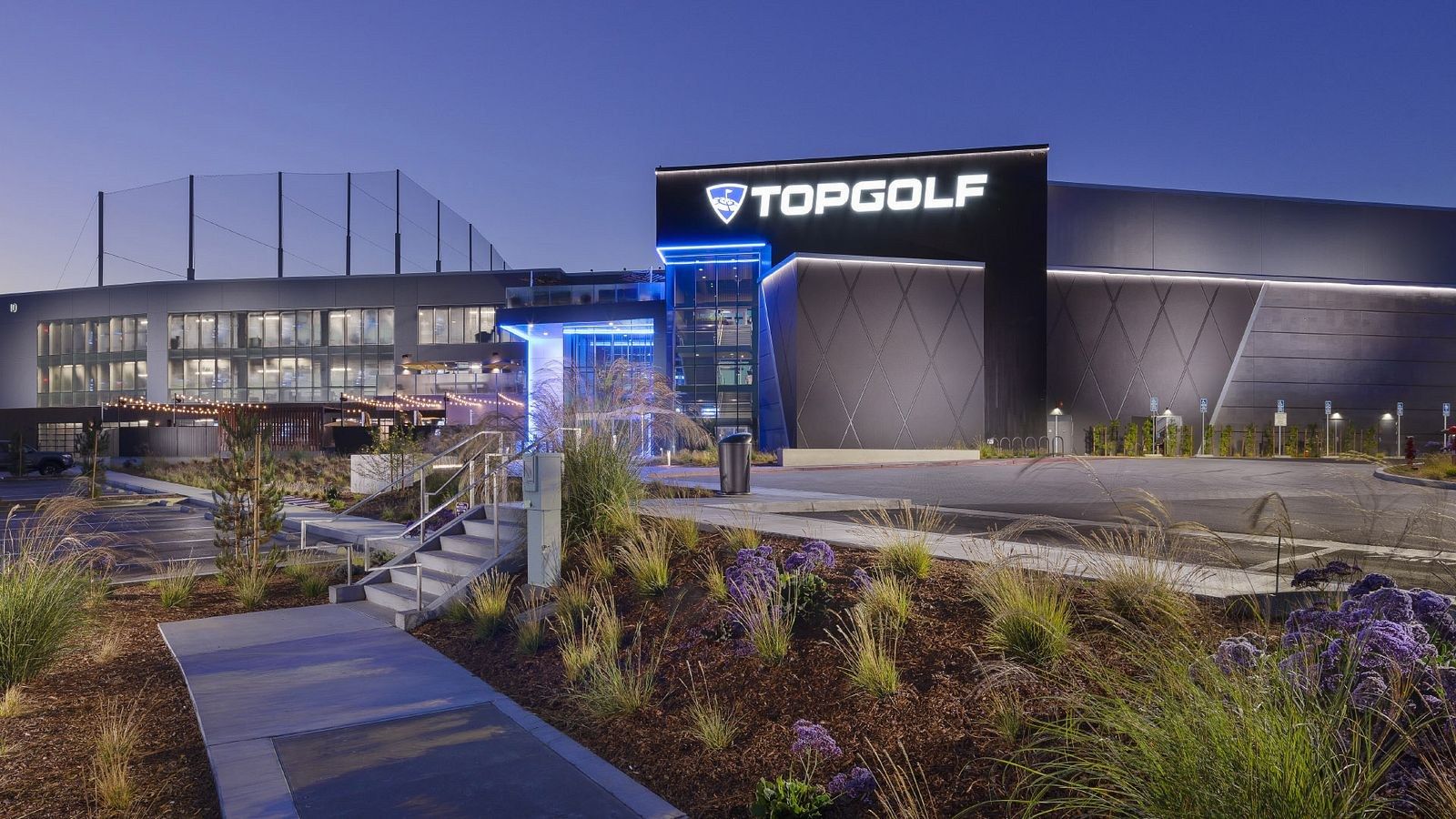 Exterior of the Topgolf venue with its sign above a multi-level building at dusk