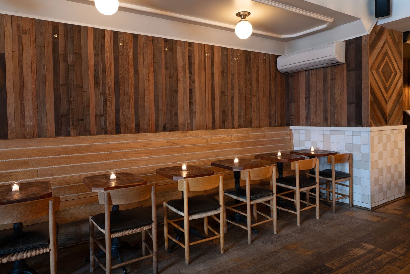Narrow bar room with wood-paneled walls, a long bench and small tables with candles
