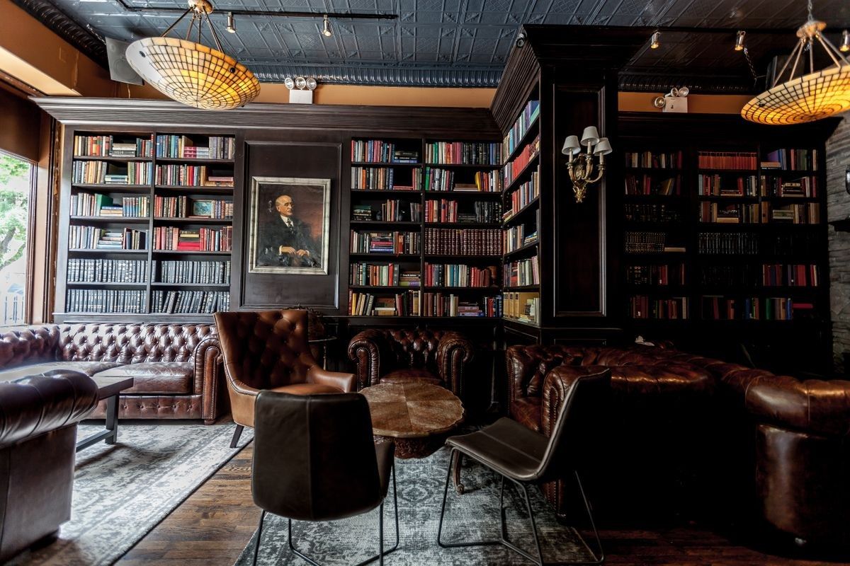 Wood-paneled library lounge with bookshelves, leather armchairs and hanging pendant lamps