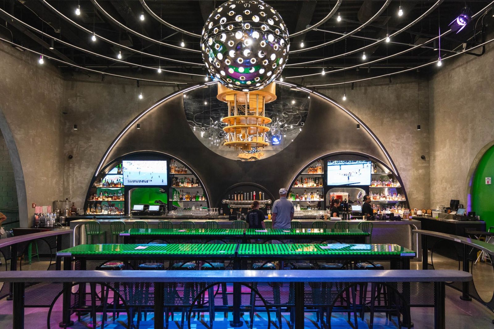 Indoor mini golf venue with a disco ball, a bar and tables under an arched ceiling