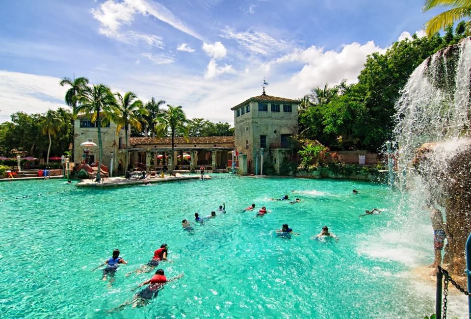 Turquoise swimming pool with waterfall and a Mediterranean-style tower, swimmers in the water