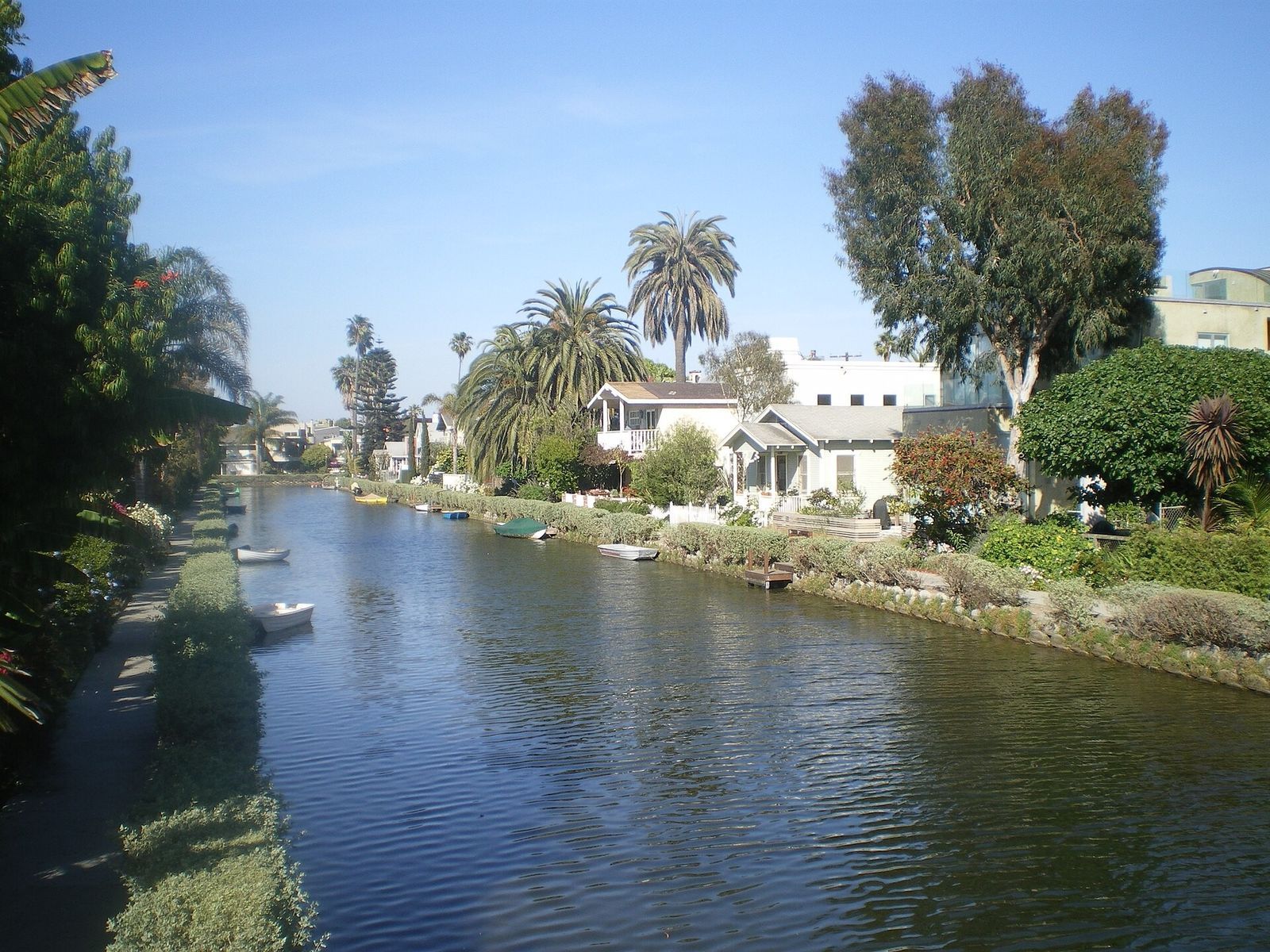 A calm canal lined with trees and small houses under a blue sky.