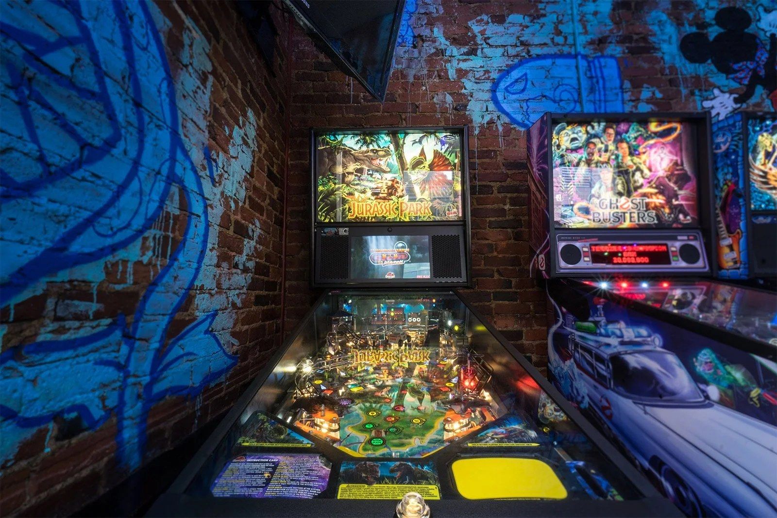 Narrow room with a graffiti mural wall and a row of lit pinball machines