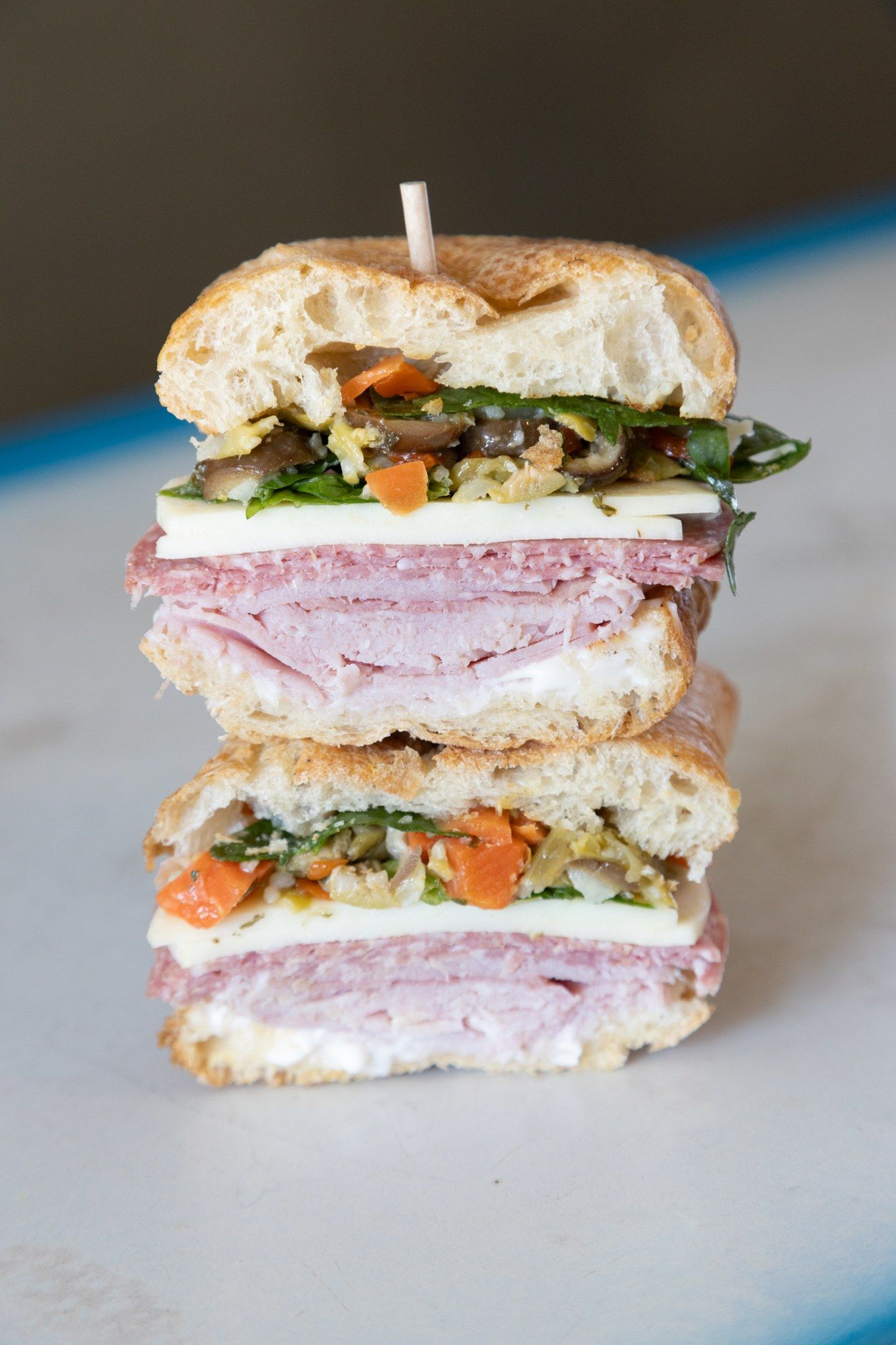 A sandwich cut in half and stacked, showing layers of sliced meat, cheese and vegetables.