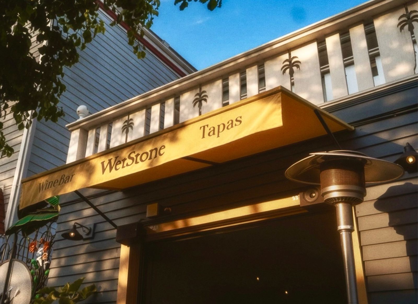 A building front with a wooden sign reading WetStone Tapas under an awning, beside a patio heater.
