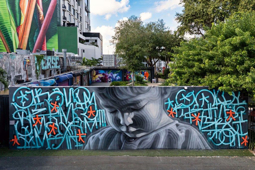 Large graffiti mural of a face among trees and murals in Wynwood