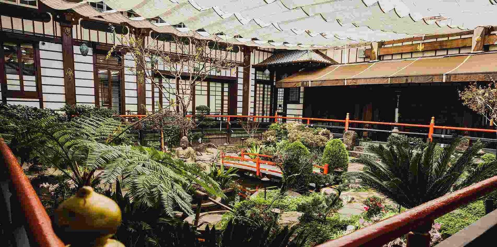 A Japanese-style building with tiled roofs and a garden courtyard with palms below.